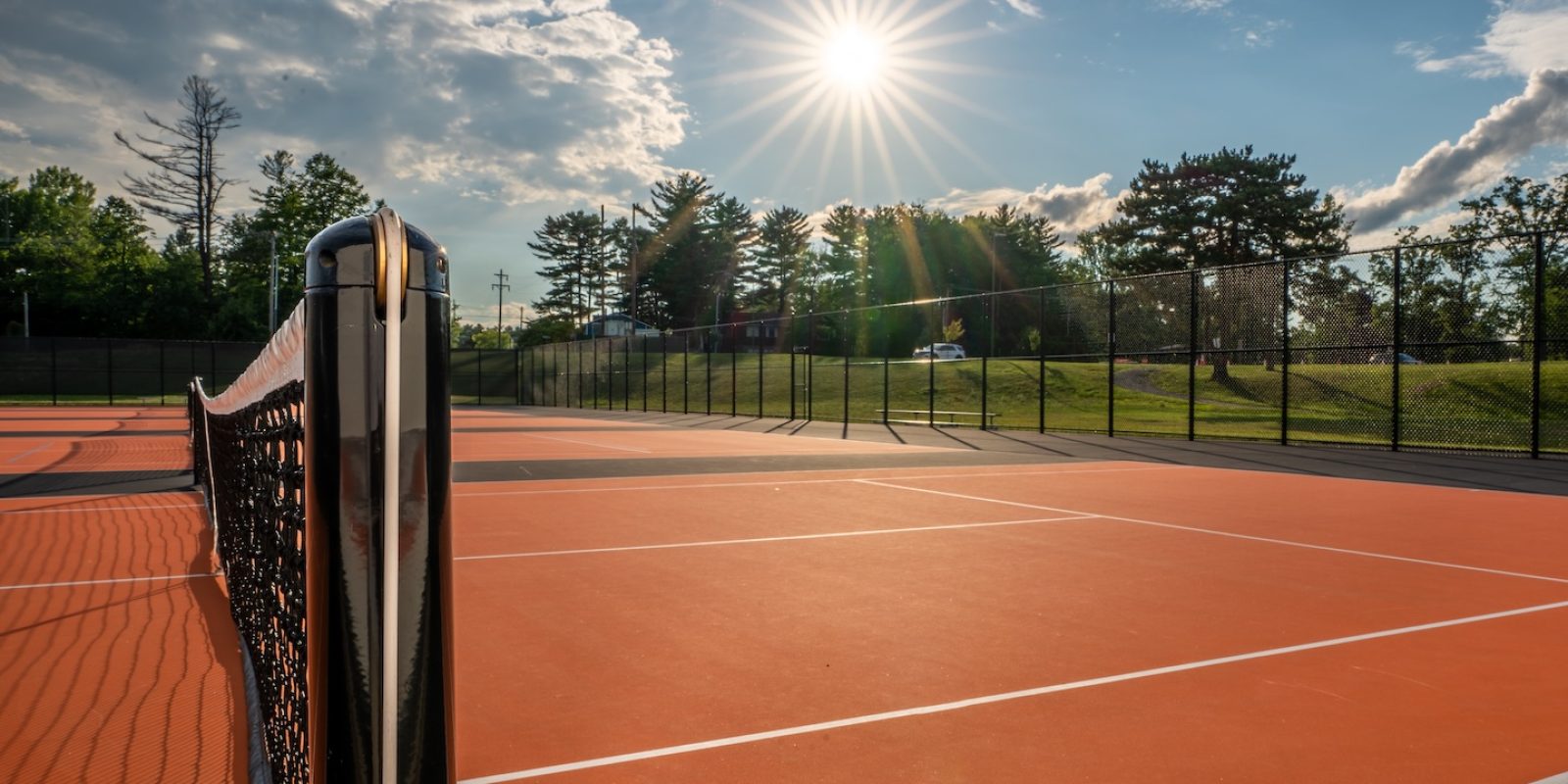 Tennis court net and post on orange and black tennis court - pickleball court with white baseline and black out of bounds